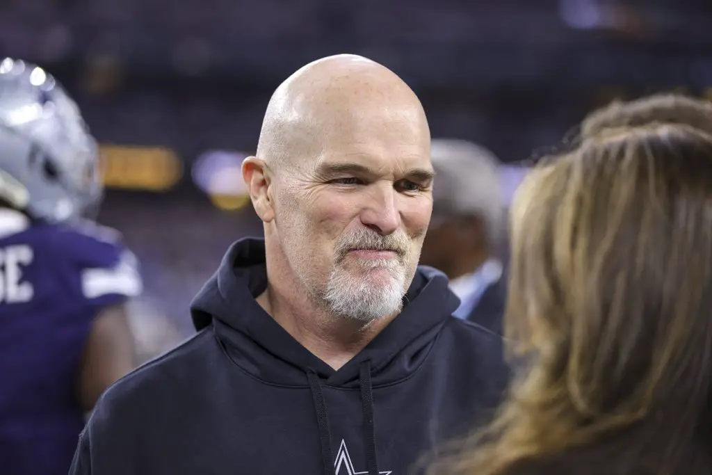 FootballR - NFL - Diese Beschreibung wurde automatisch generiert. Dan Quinn, der Head Coach der Washington Commanders, trug einen schwarzen Kapuzenpullover und unterhielt sich mit einem anderen Mann.