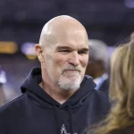 FootballR - NFL - Diese Beschreibung wurde automatisch generiert. Dan Quinn, der Head Coach der Washington Commanders, trug einen schwarzen Kapuzenpullover und unterhielt sich mit einem anderen Mann.