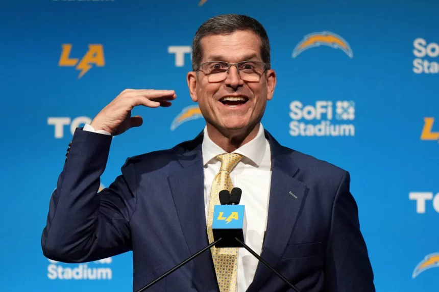 FootballR - NFL Head Coaches - Diese Beschreibung wurde automatisch generiert. Jim Harbaugh, der Cheftrainer der Chargers, zeigt in Anzug und Krawatte den Daumen nach oben.
