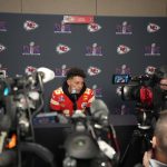 FootballR - NFL - Diese Beschreibung wurde automatisch generiert. Patrick Mahomes, der Spieler der Kansas Chiefs, ist bei einer Pressekonferenz von Reportern umgeben.