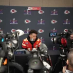 FootballR - NFL - Diese Beschreibung wurde automatisch generiert. Patrick Mahomes, der Spieler der Kansas Chiefs, ist bei einer Pressekonferenz von Reportern umgeben.