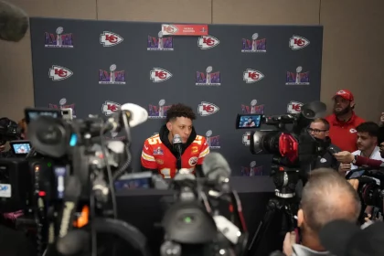 FootballR - NFL - Diese Beschreibung wurde automatisch generiert. Patrick Mahomes, der Spieler der Kansas Chiefs, ist bei einer Pressekonferenz von Reportern umgeben.