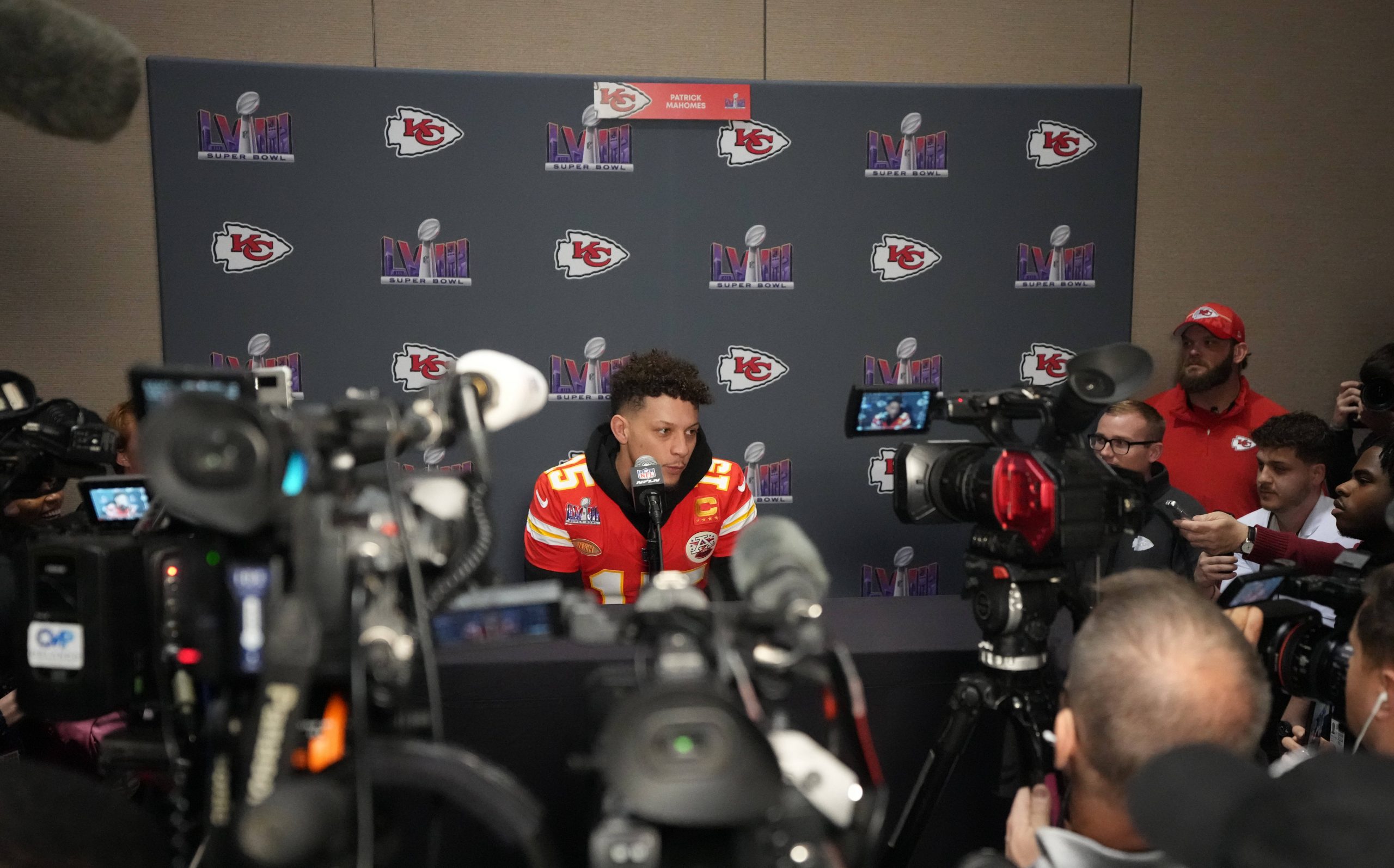 FootballR - NFL - Diese Beschreibung wurde automatisch generiert. Patrick Mahomes, der Spieler der Kansas Chiefs, ist bei einer Pressekonferenz von Reportern umgeben.