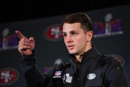 FootballR - NFL - Diese Beschreibung wurde automatisch generiert. Ein Spieler der San Francisco 49ers, Brock Purdy, zeigt während einer Super-Bowl-Pressekonferenz als Starting-QB in die Kamera.