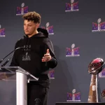 FootballR - NFL - Diese Beschreibung wurde automatisch generiert. Ein Mann, Patrick Mahomes, steht mit einer Trophäe vor sich auf einem Podium und feiert den Sieg im Super Bowl LVIII mit rekordverdächtiger Zuschauerzahl.