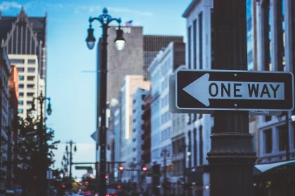 FootballR - NFL - Ein Einbahnstraßenschild vor einem städtischen Hintergrund mit verschwommenen Gebäuden und Straßenlaternen, das die Essenz des Stadtlebens in der Abenddämmerung einfängt. Diese Beschreibung wurde automatisch generiert.