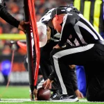 FootballR - NFL Hawk Eye - Diese Beschreibung wurde automatisch generiert. Ein NFL-Schiedsrichter kniet auf dem Spielfeld und nutzt dabei High-Tech Tracking Geräte.