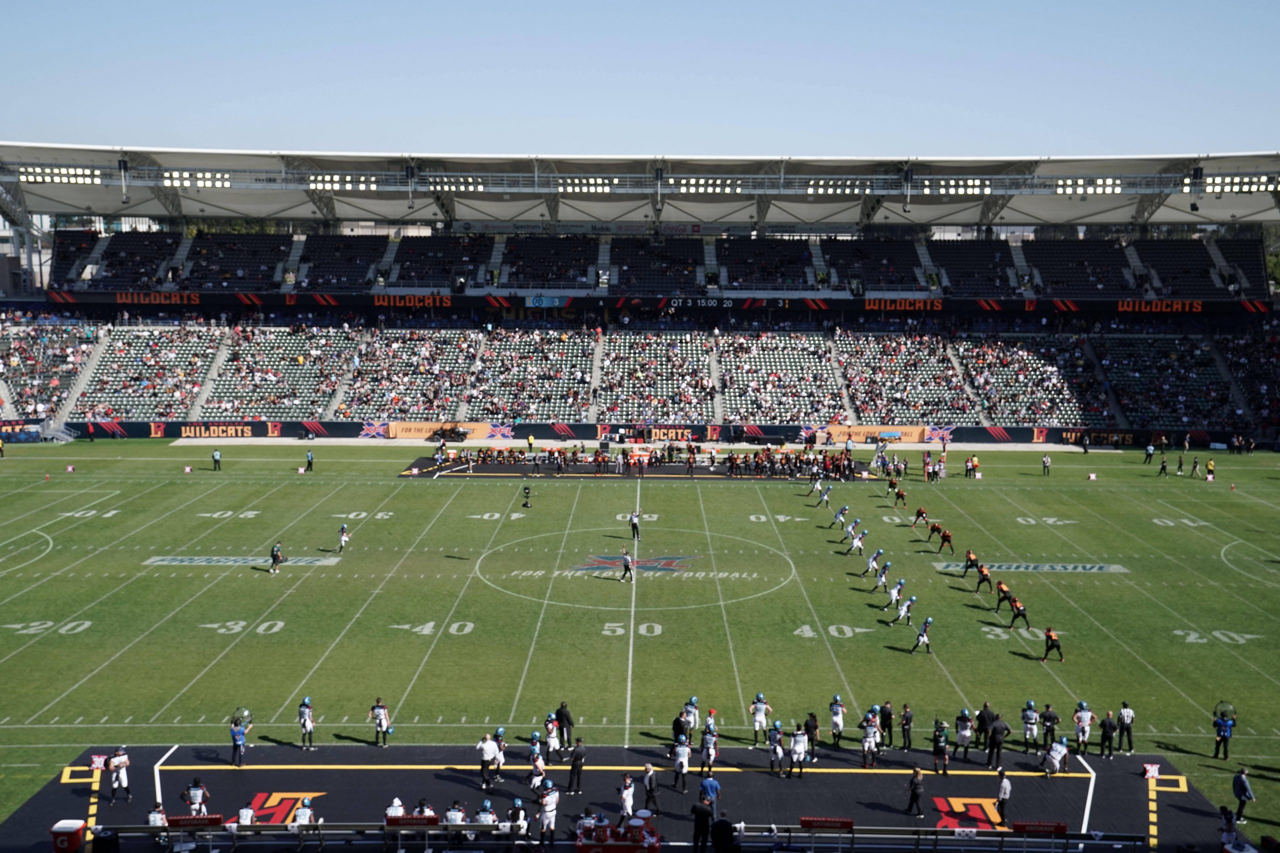 FootballR - NFL Regeländerungen - Kickoff - In einem Stadion findet gerade ein American-Football-Spiel statt, die Mannschaften stehen für den Anpfiff auf dem Spielfeld aufgereiht und die Tribünen sind unter strahlend blauem Himmel mit Zuschauern gefüllt. Diese Beschreibung wurde automatisch generiert.