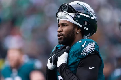 FootballR - NFL - Ein American-Football-Spieler, Haason Reddick, der jetzt die Ausrüstung der New York Jets trägt, posiert aufmerksam auf dem Spielfeld und strahlt vor dem Spiel Konzentration und Entschlossenheit aus. Diese Beschreibung wurde automatisch generiert.