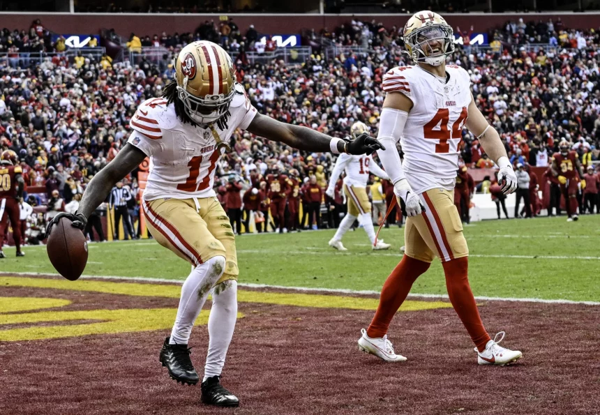 FootballR - NFL - Zwei Footballspieler in weißen und roten 49ers-Uniformen feiern auf dem Spielfeld; einer (Brandon Aiyuk) streckt triumphierend seinen Arm aus, während er den Ball hält, möglicherweise nach einem erfolgreichen Spiel. Diese Beschreibung wurde automatisch generiert.