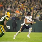 FootballR - NFL - Diese Beschreibung wurde automatisch generiert. Quarterback Justin Fields weicht einem Tackle während eines Footballspiels aus.