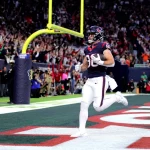 FootballR - NFL - Diese Beschreibung wurde automatisch generiert. Ein Footballspieler, Dalton Schultz, läuft mit einem Ball in der Hand.