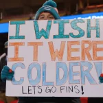 FootballR - NFL - Diese Beschreibung wurde automatisch generiert. Es drohen Amputationen! Eine Person hält ein Dolphins-Schild.