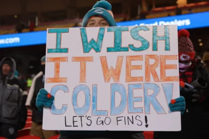 FootballR - NFL - Diese Beschreibung wurde automatisch generiert. Es drohen Amputationen! Eine Person hält ein Dolphins-Schild.