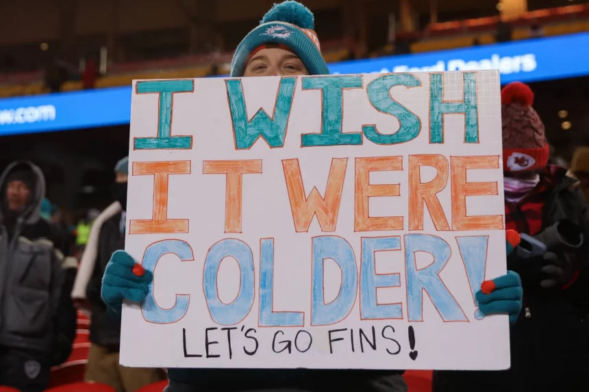 FootballR - NFL - Diese Beschreibung wurde automatisch generiert. Es drohen Amputationen! Eine Person hält ein Dolphins-Schild.