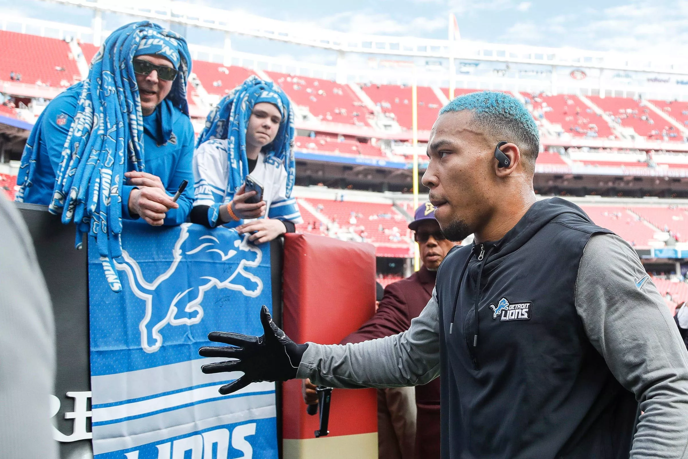 FootballR - NFL - Diese Beschreibung wurde automatisch generiert. Ein Mann mit blauem Hut unterhält sich mit Fans bei einem Footballspiel der Detroit Lions. Amon-Ra St. Brown