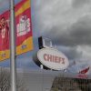 FootballR - NFL - Chiefs vor Umzug? Stadion unter einem dramatisch bewölkten Himmel mit leuchtenden Bannern der Kansas City Chiefs, die Teamgeist zeigen, flankiert vom ikonischen Ford-Branding über dem Eingang, das die jüngste Stadionrenovierung symbolisiert. Diese Beschreibung wurde automatisch generiert.