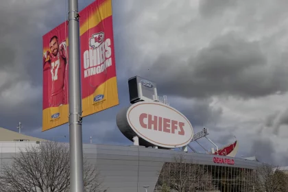 FootballR - NFL - Chiefs vor Umzug? Stadion unter einem dramatisch bewölkten Himmel mit leuchtenden Bannern der Kansas City Chiefs, die Teamgeist zeigen, flankiert vom ikonischen Ford-Branding über dem Eingang, das die jüngste Stadionrenovierung symbolisiert. Diese Beschreibung wurde automatisch generiert.