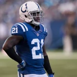 FootballR - NFL - Vontae Davis - Ein entschlossener Pro Bowler im blau-weißen Trikot #21 der Indianapolis Colts und mit Helm blickt über das Feld, konzentriert und bereit für den nächsten Spielzug. Diese Beschreibung wurde automatisch generiert.