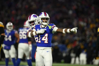 FootballR - NFL - Ein Footballspieler, Stefon Diggs, im Trikot mit der Nummer 84 gestikuliert während eines Nachtspiels auf dem Feld, während im Hintergrund seine Teamkollegen unter hellen Stadionlichtern nach einem Blockbuster-Trade zu sehen sind. Diese Beschreibung wurde automatisch generiert.