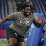 FootballR - NFL - Ein Sportler zeigt bei einem Scouting-Event in einem Stadion seine Beweglichkeits- und Schnelligkeitsübungen. Er trägt ein graues Sportshirt mit der Aufschrift „T'Vondre Sweat“, was auf seine Position als Defensive Lineman und seine Teilnehmernummer hinweist. Diese Beschreibung wurde automatisch generiert.