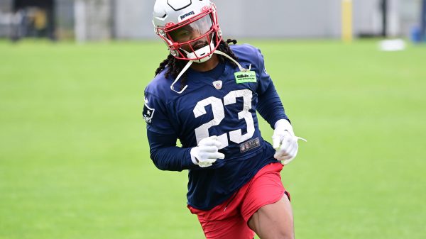 FootballR - NFL - Kyle Dugger, ein American-Football-Safety für die New England Patriots, trägt die Nummer 23, trainiert auf dem Feld, trägt einen weißen Helm, ein blaues Trikot und rote Shorts, konzentriert und Diese Beschreibung wurde automatisch generiert.