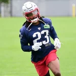 FootballR - NFL - Kyle Dugger, ein American-Football-Safety für die New England Patriots, trägt die Nummer 23, trainiert auf dem Feld, trägt einen weißen Helm, ein blaues Trikot und rote Shorts, konzentriert und Diese Beschreibung wurde automatisch generiert.