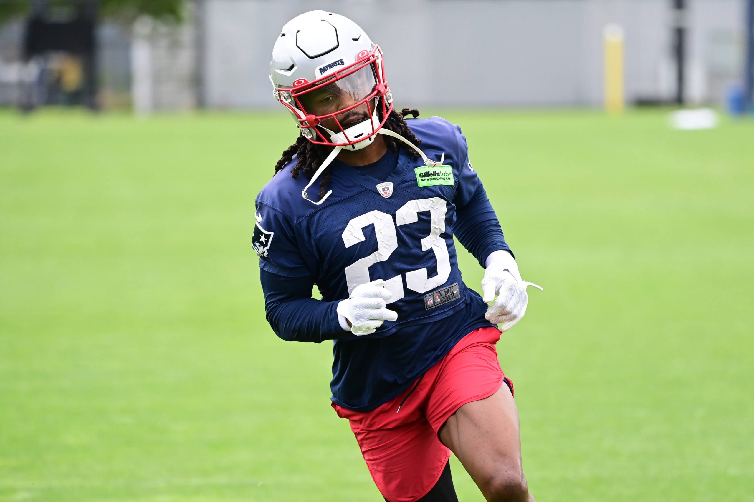 FootballR - NFL - Kyle Dugger, ein American-Football-Safety für die New England Patriots, trägt die Nummer 23, trainiert auf dem Feld, trägt einen weißen Helm, ein blaues Trikot und rote Shorts, konzentriert und Diese Beschreibung wurde automatisch generiert.