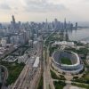 FootballR - NFL - Luftaufnahme von Chicago mit der Skyline mit hoch aufragenden Wolkenkratzern, dem Michigansee, Soldier Field, der Heimat der Chicago Bears, und mehreren zusammenlaufenden Bahngleisen an einem bewölkten Tag. Diese Beschreibung wurde automatisch generiert.