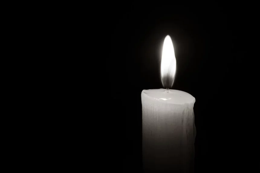 Jeremiah Kelly - NFL - Mason Alexander - Eine einzelne weiße Kerze, an deren Seite geschmolzenes Wachs heruntertropft, brennt hell vor einem pechschwarzen Hintergrund. Die Flamme ist gleichmäßig und leuchtend, wirft einen sanften Schein um die Kerze und beleuchtet ihre wachsartige Oberfläche. Der starke Kontrast, ähnlich wie Jim Ottos Vermächtnis als Mr. Raider, betont das zarte Licht der Kerze. Diese Beschreibung wurde automatisch generiert.