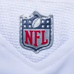 NFL Spielplan 2026 - 2025 Preseason -Rivalries Trikots - NFL-Fanartikel - NFL Spielplan 2025 - Nahaufnahme des NFL Spielplan 2024 -Logos auf einem weißen Footballtrikot. Das Logo zeigt ein Muster der amerikanischen Flagge mit Sternen und Streifen, ein Football-Symbol und fettgedruckte rote „NFL“-Buchstaben vor Diese Beschreibung wurde automatisch generiert.