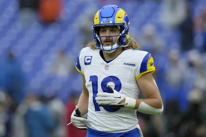 FootballR - NFL - Ben Skowronek - Ein professioneller Footballspieler, der eine blau-gelbe Uniform der Los Angeles Rams mit der Nummer 10 trägt, läuft über das Feld. Er hat blondes, lockiges Haar unter seinem blauen Helm mit einem Rams-Logo. Im Hintergrund ist ein großes, offenes Stadion mit blauen Sitzplätzen zu sehen. Diese Beschreibung wurde automatisch generiert.