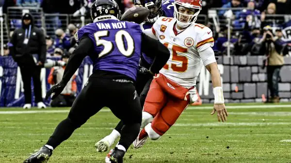 FootballR - NFL Saison 2024 - Der Quarterback der Kansas City Chiefs in einer rot-weißen Uniform weicht während eines spannenden NFL-Spiels einem Tackle eines Spielers der Baltimore Ravens im lila Trikot mit der Nummer 50 und dem Namen „Van Noy“ aus. Diese Beschreibung wurde automatisch generiert.