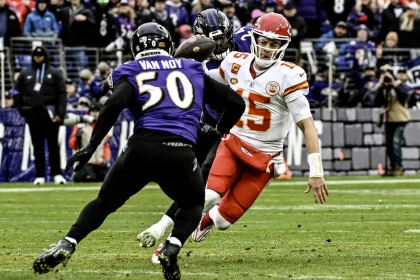 FootballR - NFL Saison 2024 - Der Quarterback der Kansas City Chiefs in einer rot-weißen Uniform weicht während eines spannenden NFL-Spiels einem Tackle eines Spielers der Baltimore Ravens im lila Trikot mit der Nummer 50 und dem Namen „Van Noy“ aus. Diese Beschreibung wurde automatisch generiert.