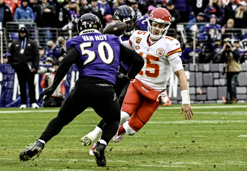 FootballR - NFL Saison 2024 - Der Quarterback der Kansas City Chiefs in einer rot-weißen Uniform weicht während eines spannenden NFL-Spiels einem Tackle eines Spielers der Baltimore Ravens im lila Trikot mit der Nummer 50 und dem Namen „Van Noy“ aus. Diese Beschreibung wurde automatisch generiert.
