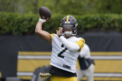 FootballR - NFL - Ein Footballspieler mit schwarzem Helm und weiß-gelbem Trikot mit der Nummer 2, der Quarterback Justin Fields ähnelt, ist mitten in einer Wurfbewegung. Er ist von einem grünen Übungsplatz im Freien umgeben, im Hintergrund ist eine weitere Person zu sehen. Die Szene scheint eine Trainings- oder Übungseinheit der Steelers zu sein. Diese Beschreibung wurde automatisch generiert.