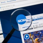 College Footballer - NFL - Eine Lupe konzentriert sich auf das NCAA Logo, das auf einem Computerbildschirm angezeigt wird, und hebt in den Browser-Tabs verschiedene Abschnitte wie „Sport“, „Schulen“ und „Meisterschaften“ hervor. Unter dem Logo gibt es einen Zeitplan für Footballspiele und ein Video-Thumbnail mit einem Spieler in orange-weißer Uniform, was die umfangreichen Kommerzialisierungsbemühungen der NCAA hervorhebt. Diese Beschreibung wurde automatisch generiert.