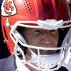 FootballR - NFL - US Präsident Joe Biden trägt einen roten Footballhelm mit dem Logo der Kansas City Chiefs an der Seite. Der Gesichtsschutz ist weiß und der Helm ist signiert. Die Person, die Joe Biden verblüffend ähnlich sieht, trägt ebenfalls einen dunklen Anzug, während von einer anderen Person im Hintergrund nur ein Teil zu sehen ist. Diese Beschreibung wurde automatisch generiert.