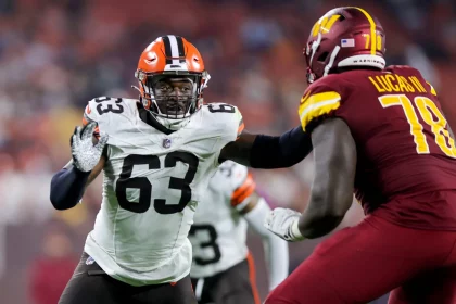FootballR - NFL - Ein Spieler der Cleveland Browns in weißem Trikot und orangefarbenem Helm (Nummer 63) versucht, Lonnie Phelps von den Washington Commanders in roter Uniform (Nummer 78) während eines NFL-Spiels zu blockieren. Die Szene fängt die intensive Action auf dem Spielfeld ein, mit verschwommenen Zuschauern im Hintergrund. Diese Beschreibung wurde automatisch generiert.
