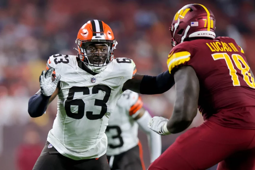 FootballR - NFL - Ein Spieler der Cleveland Browns in weißem Trikot und orangefarbenem Helm (Nummer 63) versucht, Lonnie Phelps von den Washington Commanders in roter Uniform (Nummer 78) während eines NFL-Spiels zu blockieren. Die Szene fängt die intensive Action auf dem Spielfeld ein, mit verschwommenen Zuschauern im Hintergrund. Diese Beschreibung wurde automatisch generiert.