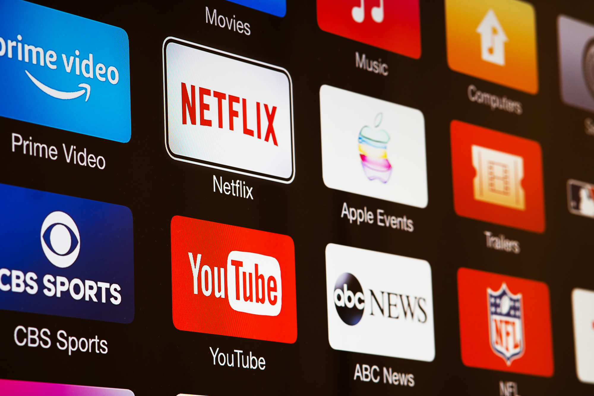 NFL in Brasilien - NFL Sunday Ticket - Auf einem Fernsehbildschirm werden verschiedene App-Symbole angezeigt, darunter Prime Video, Netflix, CBS Sports, YouTube und ABC News. Weitere sichtbare Symbole sind Filme, Musik, Computer, Trailer, Apple Events und das NFL Sunday Ticket-Logo – was die vielfältigen Multimedia-Optionen in der Streaming-Revolution hervorhebt. Diese Beschreibung wurde automatisch generiert.