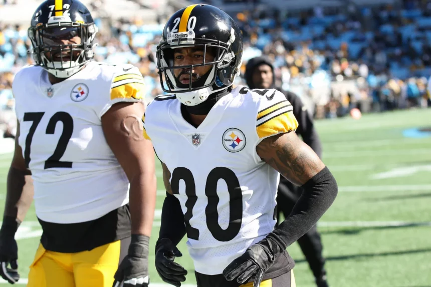 FootballR - NFL - Cameron Sutton - Zwei American-Football-Spieler der Pittsburgh Steelers stehen auf dem Spielfeld. Der Spieler im Vordergrund, Cameron Sutton, trägt ein weiß-gelbes Trikot mit der Nummer 20, während der Spieler hinter ihm die Nummer 72 trägt. Sie stehen auf einem Footballfeld mit einer verschwommenen Stadionmenge im Hintergrund. Diese Beschreibung wurde automatisch generiert.