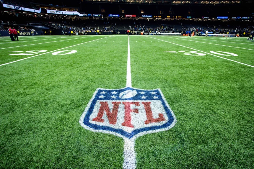 FootballR - NFL Saison 2024 - Ein Footballfeld mit dem NFL-Logo in der Mitte zwischen der 20- und 30-Yard-Linie. Das Stadion ist beleuchtet und im Hintergrund voller Zuschauer. Eine Anzeigetafel zeigt „FINAL STATS“ für die Saison 2023 an. Das Feld hat deutlich erkennbare weiße Yard-Linien und Hash-Markierungen, was auf eine gut gepflegte Spielfläche hinweist. Diese Beschreibung wurde automatisch generiert.