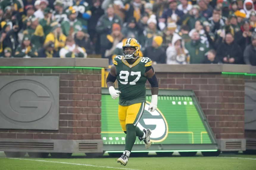 FootballR - NFL Kenny Clark - Ein Footballspieler der Green Bay Packers in grün-gelber Uniform mit der Nummer 97 rennt auf das Spielfeld. Der Defense Star steht vor einem Hintergrund jubelnder Fans, von denen viele Packers-Kleidung tragen. Auf der Backsteinmauer im Hintergrund ist ein großes „G“-Logo zu sehen. Diese Beschreibung wurde automatisch generiert.