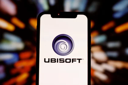 FootballR - NFL Primetime Fantasy - Ein Smartphone mit dem Ubisoft-Logo auf dem Bildschirm. Das Logo, ein blaues Spiraldesign mit der Aufschrift „UBISOFT“ darunter, fällt deutlich auf. Der Hintergrund ist mit mehrfarbigen Lichtstreifen verschwommen, was einen dynamischen und lebendigen Effekt rund um das Telefon erzeugt, der an ein intensives Live-Action-Fantasy-Spiel der NFL Primetime erinnert. Diese Beschreibung wurde automatisch generiert.
