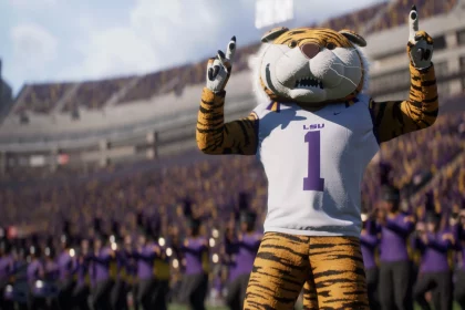 FootballR - NFL College Football 26 - Ein Tiger-Maskottchen, das triumphierend auf das College-Footballfeld zurückkehrt, trägt ein weißes Trikot mit der Nummer 1 und „LSU“ und steht mit beiden Zeigefingern nach oben auf einem Footballfeld. Im Hintergrund ist ein überfülltes Stadion mit Fans in Lila und Gold sowie einer Blaskapelle in passender lila Kleidung zu sehen. Diese Beschreibung wurde automatisch generiert.