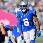 FootballR - NFL - Ein Footballspieler in einem blauen Trikot mit der Nummer 6, Quandre Diggs, und einem silbernen Helm steht während eines Titans-Spiels auf dem Feld. Im Hintergrund sind weitere Spieler zu sehen, darunter einer in einer braun-weißen Uniform. Das Stadion ist voller jubelnder Fans. Diese Beschreibung wurde automatisch generiert.