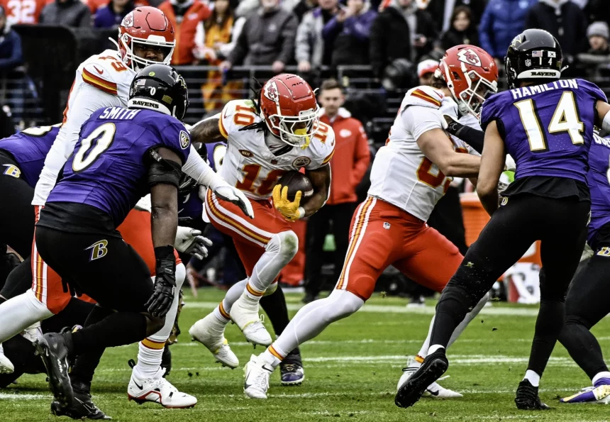 FootballR - NFL Roquan Smith - Im NFL-Saisonauftakt treffen Spieler der Kansas City Chiefs und der Baltimore Ravens auf dem Spielfeld aufeinander. Ein Chiefs-Spieler mit der Nummer 10 stürmt durch die Abwehr, während Ravens-Spieler Roquan Smith und ein weiterer Spieler mit der Nummer 14 versuchen, ihn zu blockieren. Im Hintergrund dieses spannenden Spiels zwischen den Ravens und den Chiefs jubeln begeisterte Fans. Diese Beschreibung wurde automatisch generiert.