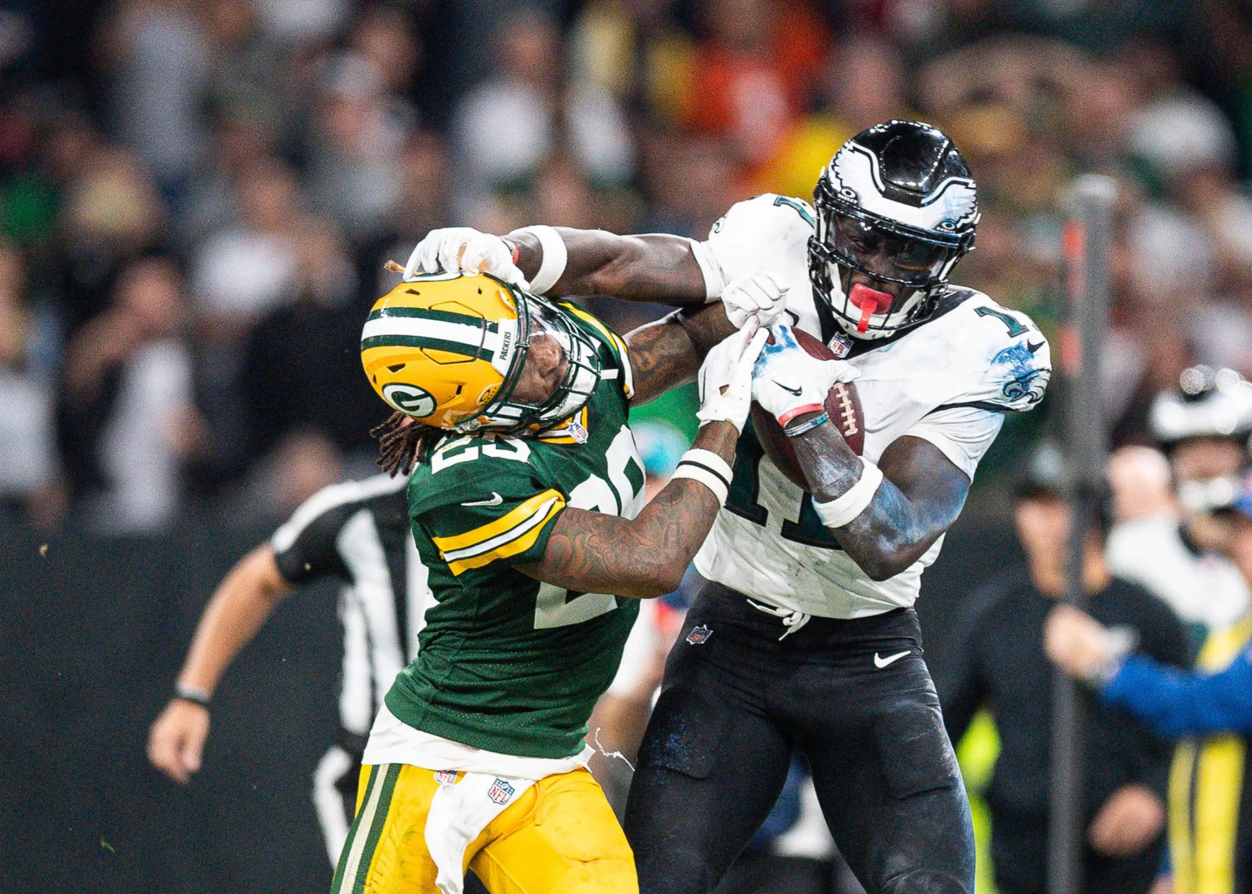 FootballR - NFL - Ein Footballspieler in weiß-grüner Uniform streckt beim Monday Night Football einen Spieler in grün-gelber Uniform mit ausgestreckten Armen aus. Der Spieler in Grün versucht, den gegnerischen Spieler A.J. Brown zu tackeln, wird dabei aber weggestoßen. Im Hintergrund ist eine Menge von Zuschauern und Offiziellen zu sehen. Diese Beschreibung wurde automatisch generiert.