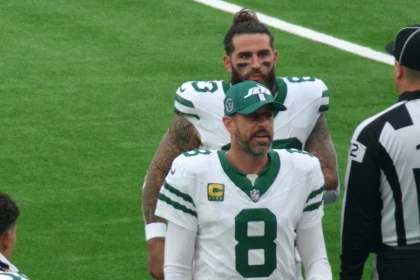 FootballR - NFL - Ein Footballspieler in weiß-grüner New York-Jets-Uniform, Nummer 8, spricht mit einem Schiedsrichter. Er trägt eine Kappe, während ein anderer Jets-Spieler mit langen Haaren und Bart hinter ihm steht. Das Spielfeld ist grün, der Schiedsrichter trägt schwarz-weiße Streifen – fast wie ein automatisch gespeicherter Entwurf. Diese Beschreibung wurde automatisch generiert.